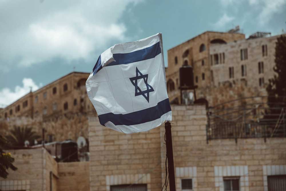 Bandeira de Israel, com Estrela de David azul em um fundo branco, entre duas faixas azuis horizontais, hasteada em rua de Jerusalém.
