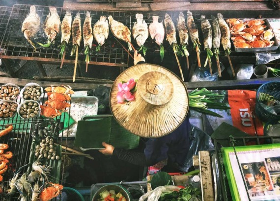 Mulher espeta um peixe ao lado de outros peixes expostos para venda em barraca de rua ambulante em Bangkok