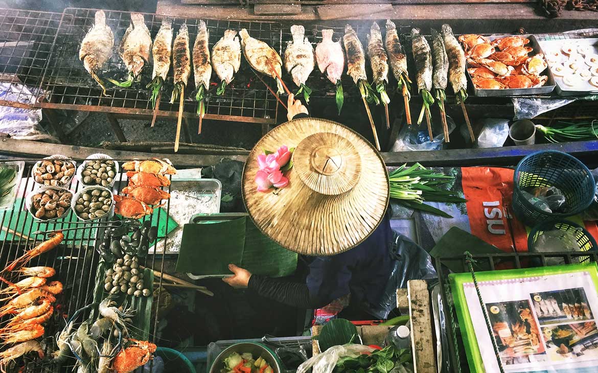 Mulher espeta um peixe ao lado de outros peixes expostos para venda em barraca de rua ambulante em Bangkok