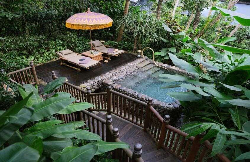 durante o dia, espreguiçadeiras em frente a piscina em varanda rodeada por árvores em um dos hotéis em Bali