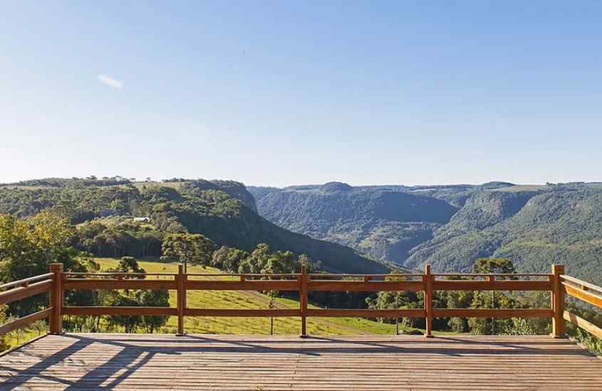 Em um dia de sol, deck de madeira do Parque Olivas de Gramado, um dos lugares para inserir no roteiro de Gramado e Canela, com montanhas e árvores ao redor