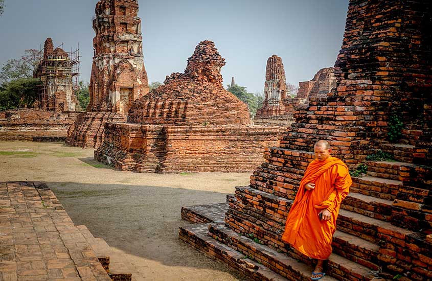 monge, com roupa laranja, caminha em terro de templo, durante o dia