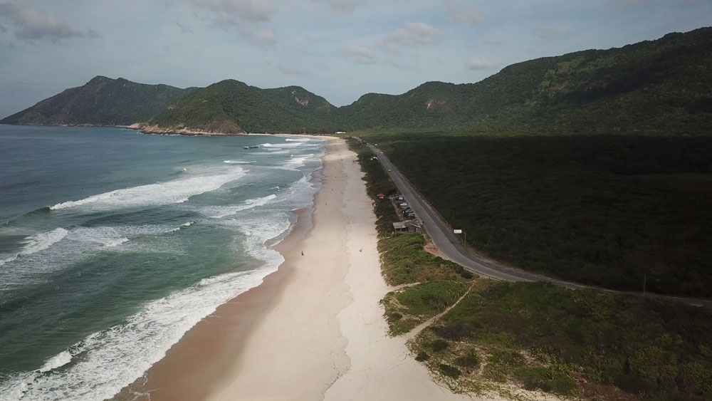 Vista área de mar, areia, montanhas e estrada em Grumari, bairro no Rio de Janeiro
