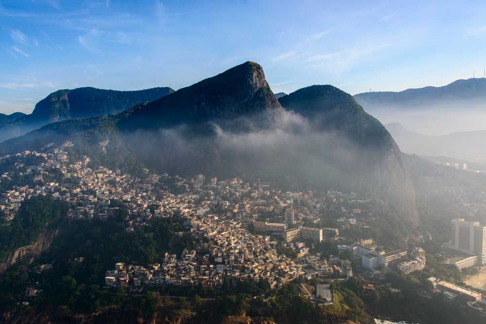 Vista área e montanhas entre nuvens, e construções em cima de morros, durante o dia, no Rio de Janeiro