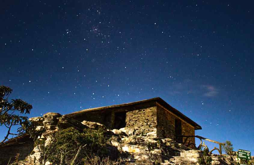 Durante a noite, casa de pedra com céus estrelado no fundo e natureza em volta