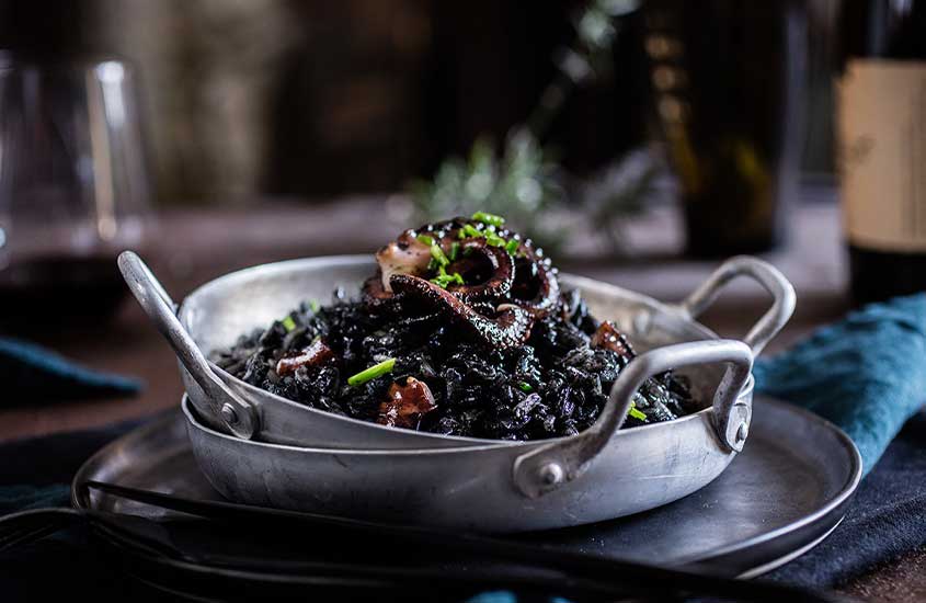 vasilha de alumínio redonda com risotto negro, um dos pratos da culinária croata que e leva lula, azeite, alho, vinho tinto