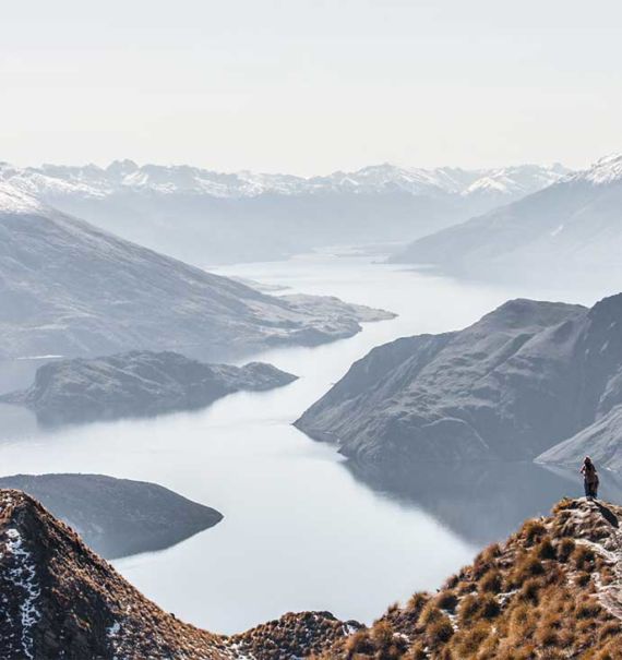 viajantes tiram fotos em cima de montanha com vista para o mar na nova Zelândia, durante o dia