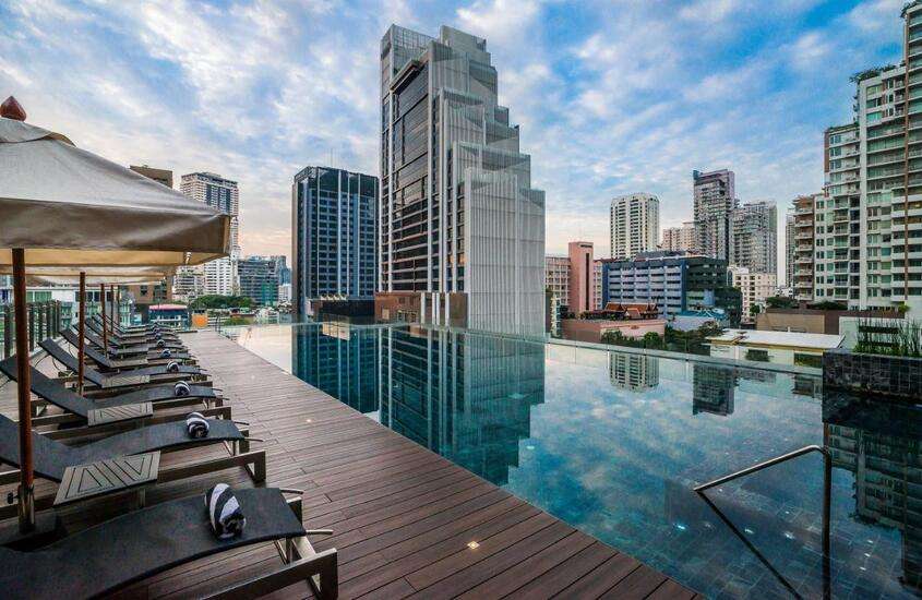 durante o dia, diversas espreguiçadeiras em deck dm frente a piscina em cobertura de hotel em Bangkok com vista da cidade
