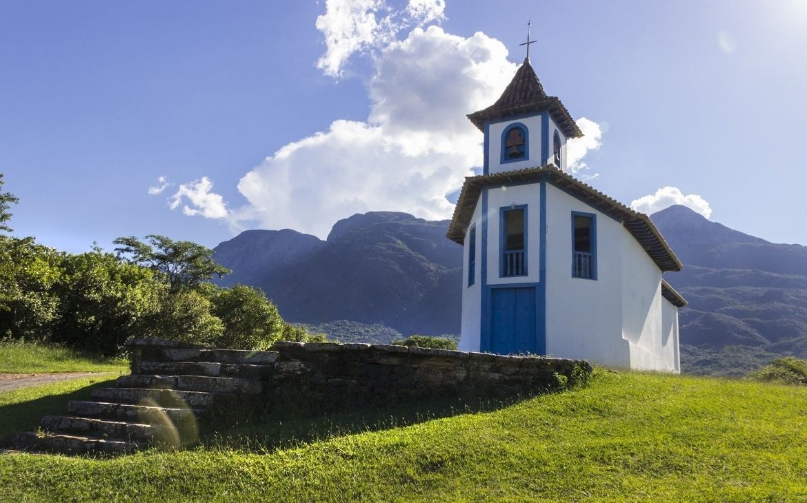 igreja branca, com porta e janelas azuis e montanhas ao fundo, durante o dia em um dos destinos em minas gerais