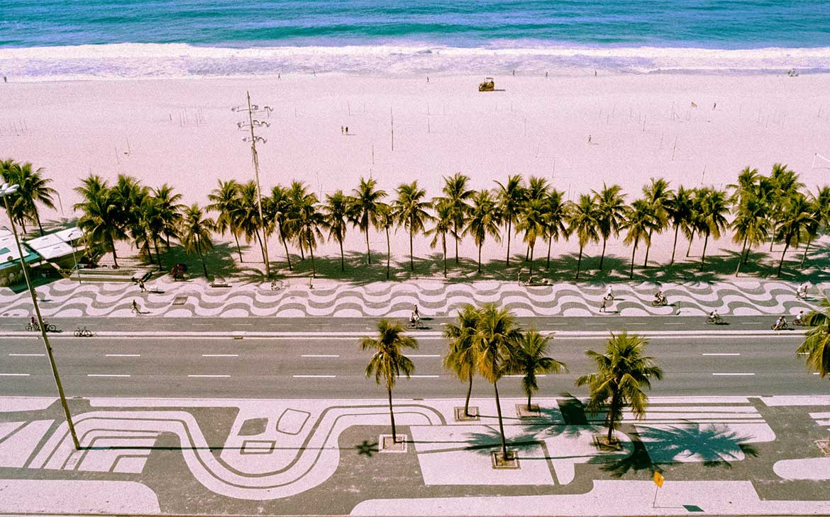 vista aérea de calçada, coqueiros, areia e mar em Copacabana, uma opção de onde ficar no rio de janeiro