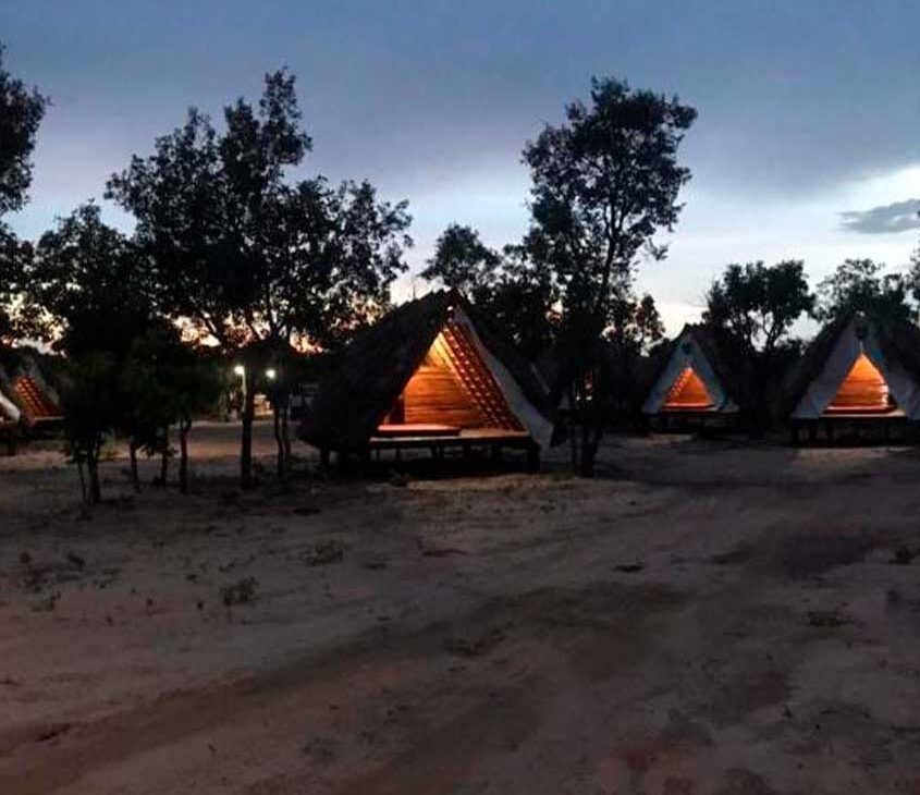 cabana com luz acessa cercada de árvores, durante o anoitecer em camping jalapão