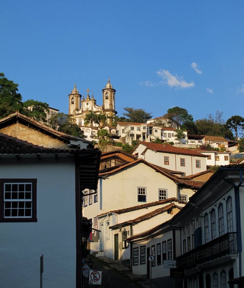 construções brancas em ladeira, onde há no topo uma igreja em Ouro Preto, um dos lugares baratos no brasil para viajar