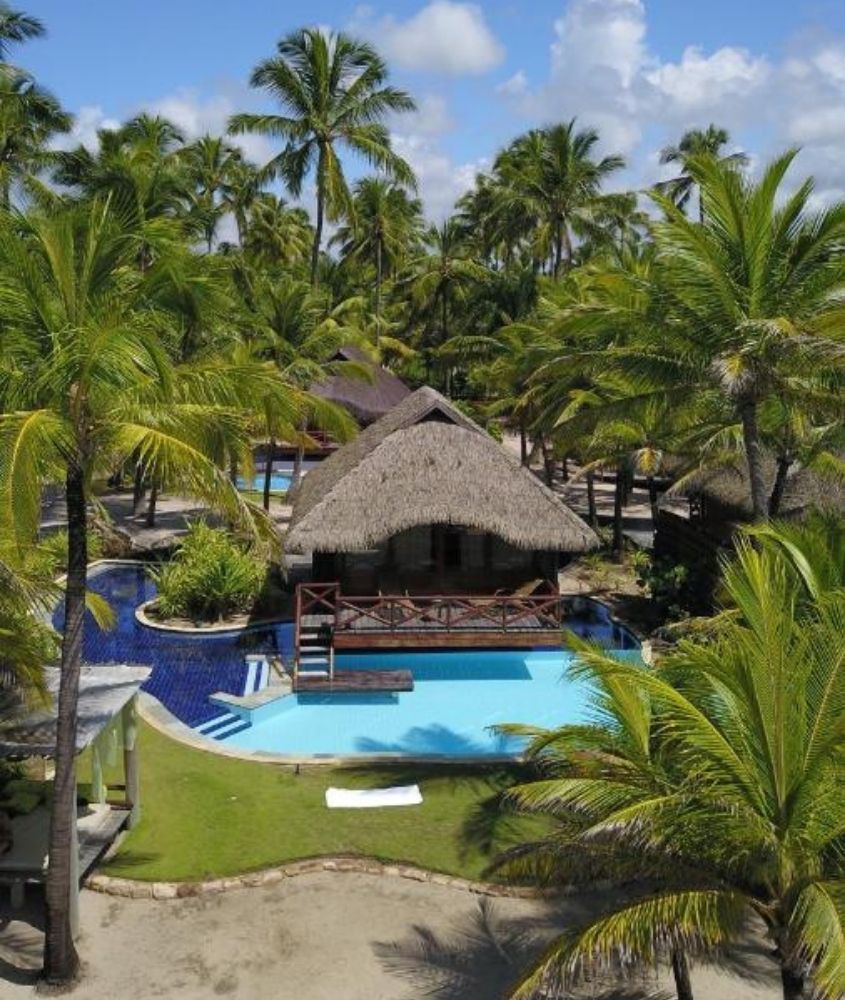 cabanas de palha em frente a piscina rodeada de coqueiros, durante dia ensolarado em nannai muro alto, um dos melhores hotéis de luxo no brasil