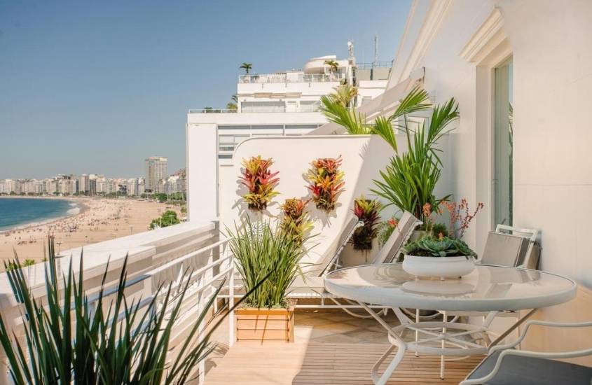 varanda de hotel copacabana palace onde há mesa, cadeiras e vasos de plantas, com vista para praia, durante dia ensolarado