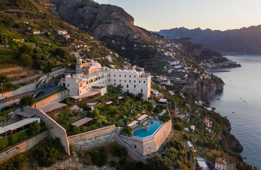 vista aérea de monastero santa rosa hotel & spa, localizado em uma montanha de frente para o mar, durante o entardecer na itália