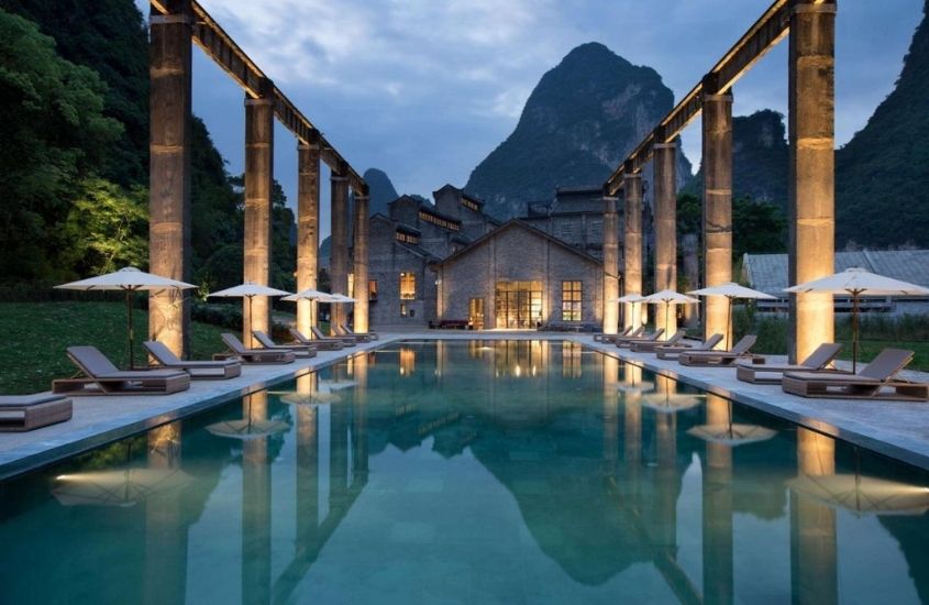piscina cerca de espreguiçadeiras, com montanha ao fundo, durante o anoitecer, em yangshuo sugar house, um dos hotéis mais bonitos do mundo