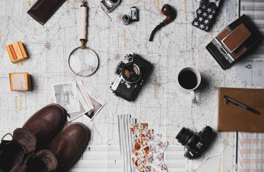 sapatos, lupa, caneca de café, fotos e câmeras em cima de mapa de papel