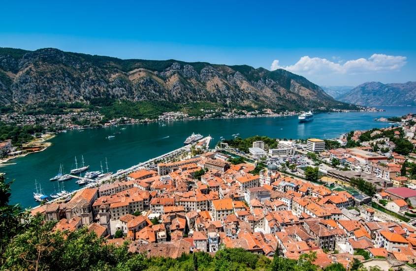 vista aérea de casas, barcos em mar e montanhas, durante o dia em montenegro um dos países baratos na europa para viajar na europa