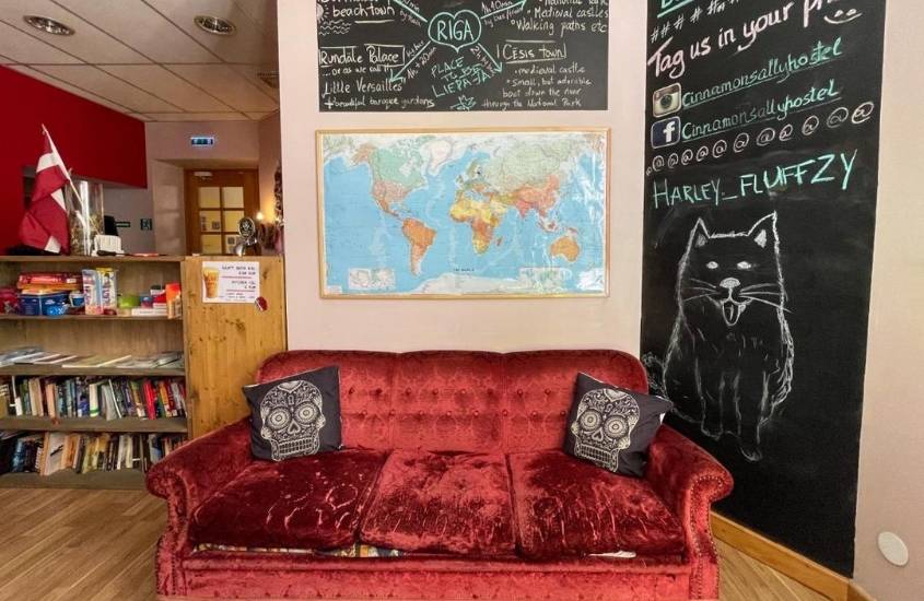 almofadas pretas com desenho de caveira em cima de sofá vermelho, em sala com prateleira de livros em hostel cinnamon sally em riga, na letônia