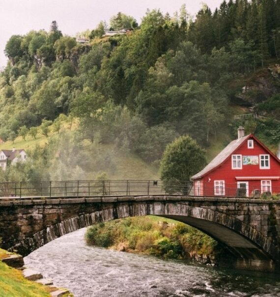 casa vermelha em ponte sobre o rio e em frente a montanha cheia de árvores, durante o dia na europa