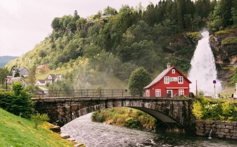 casa vermelha em ponte sobre o rio e em frente a montanha cheia de árvores, durante o dia na europa