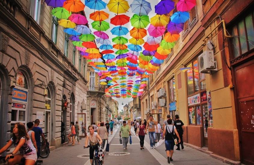 pessoas caminham sob teto com guarda-chuvas coloridos em rua da romênia, na europa