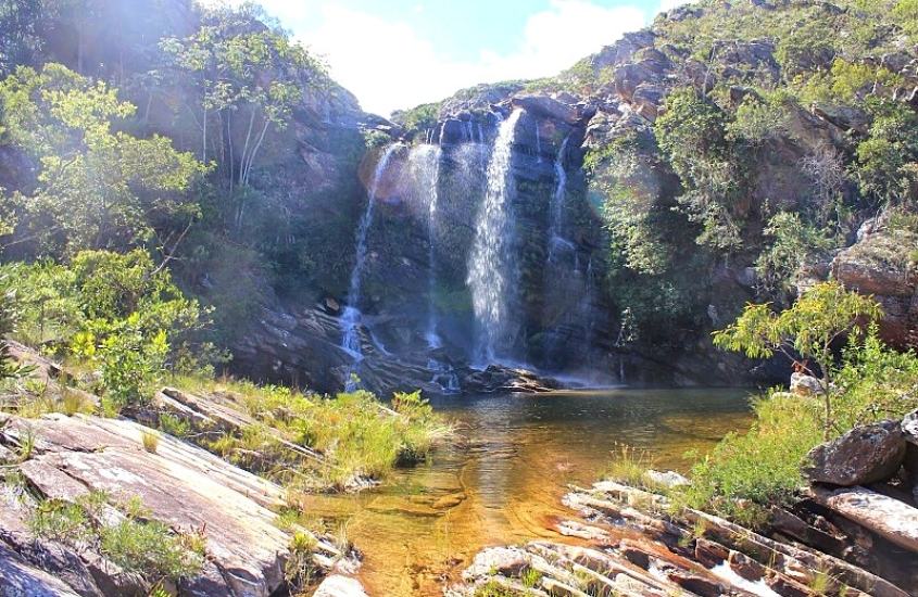 cachoeira cercada de rochas e árvores, durante dia ensolarado em serra do cipó