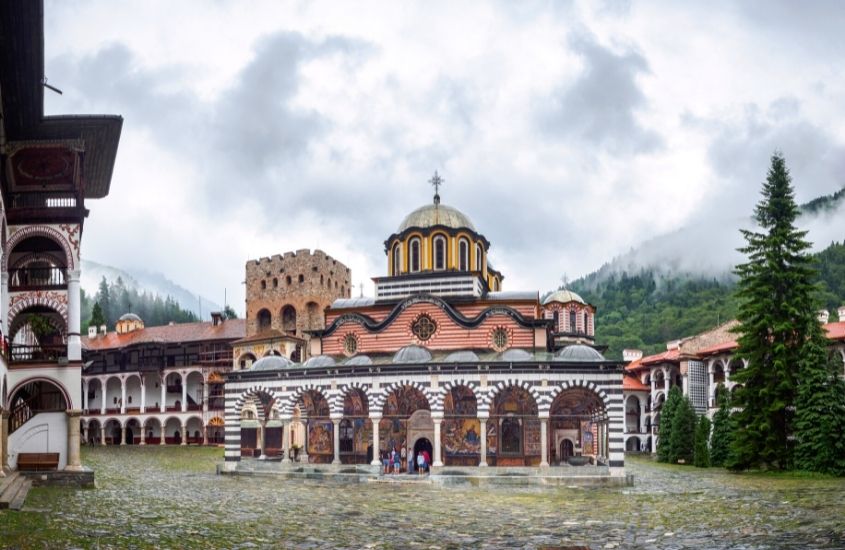 durante dia nublado, pessoas entram em mosteiro de rila, um dos pontos turísticos da bulgária