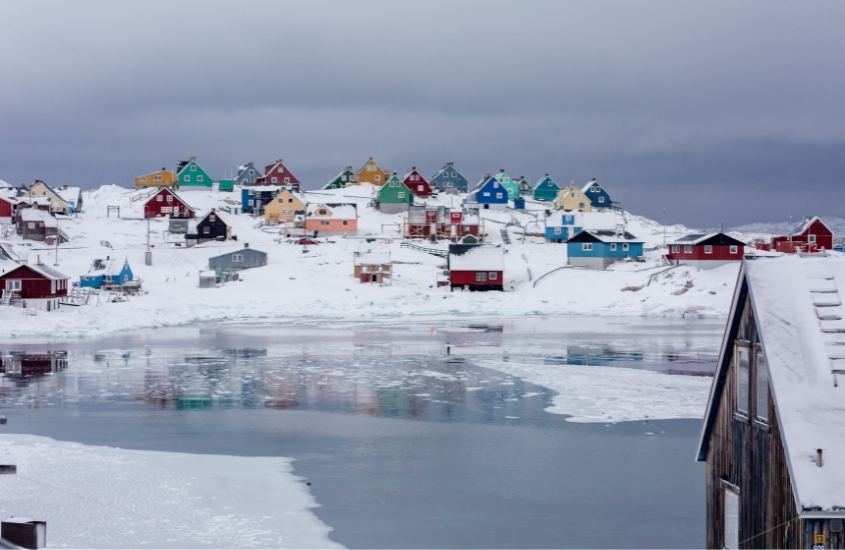 casas coloridas em morro coberto de neve, em frente a lago congelado em klinck, na groelândia