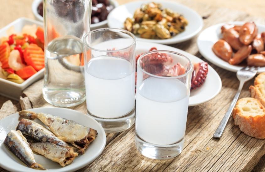 mesa onde há pratos com frutos do mar e copos com ouzo, uma bebida popular na grécia