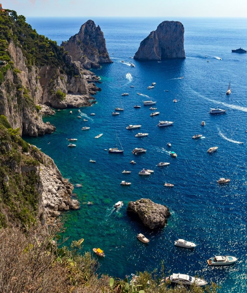vista aérea de rochas a beira mar, onde há diversos barcos, durante o dia em capri, uma das ilhas mais bonitas do mundo