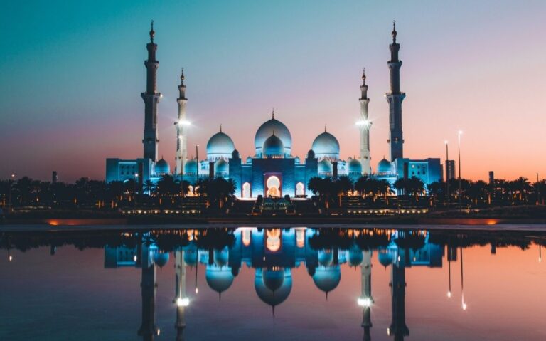 mesquita de concreto azul e bege em frente a rio, durante o entardecer, em abu dhabi, um dos lugares mais caros do mundo para viajar