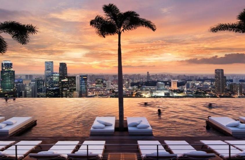 pessoas tomam banho em piscina de borda infinita com vista para a cidade, durante o entardecer em Singapura