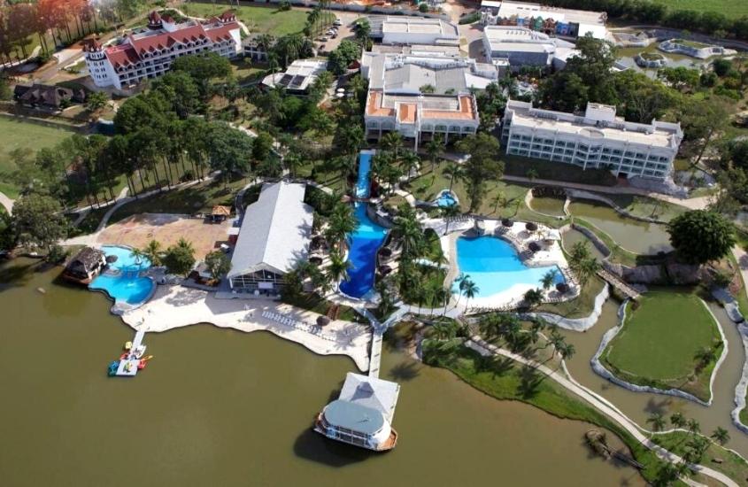 vista aérea de complexo onde funciona mavsa resort, onde há com construções, piscinas e árvores em frente a lago em cesário lange, durante o dia