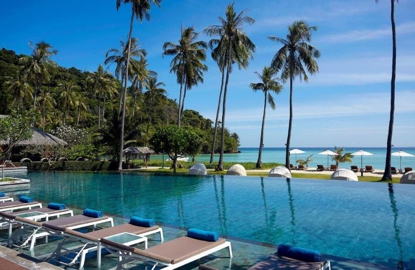 espreguiçadeiras em frente a piscina com vista para o mar, durante o dia em saii phi phi island village, uma ótima opção de resort para quem busca onde ficar em krabi