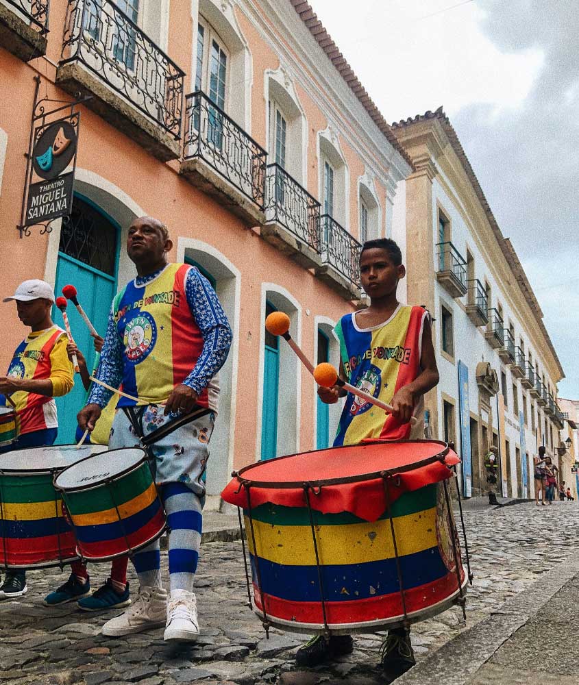 durante o dia, homens tocam tambores coloridos em ruas de paralelepido pelourinho, local histórico para incluir em um roteiro viagem nordeste