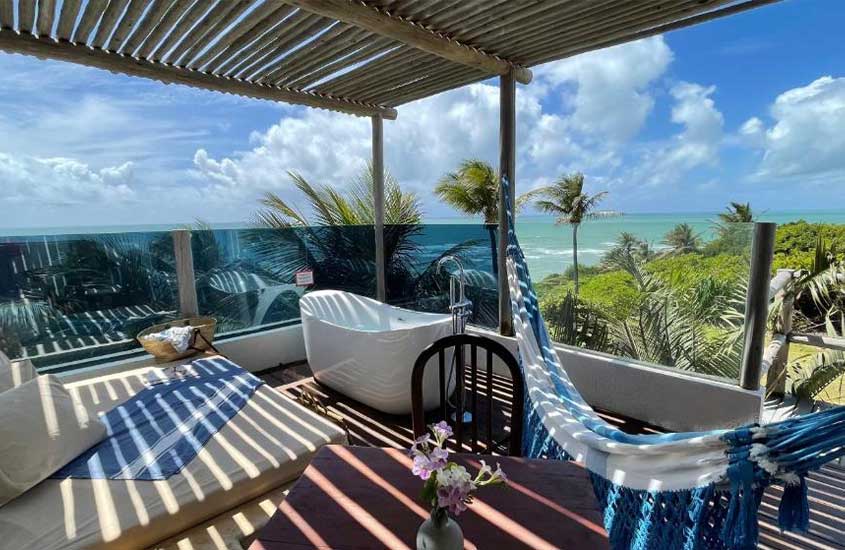 durante o dia, colchão, mesa, cadeira, rede de descanso e banheira de hidromassagem em varanda com vista para o mar