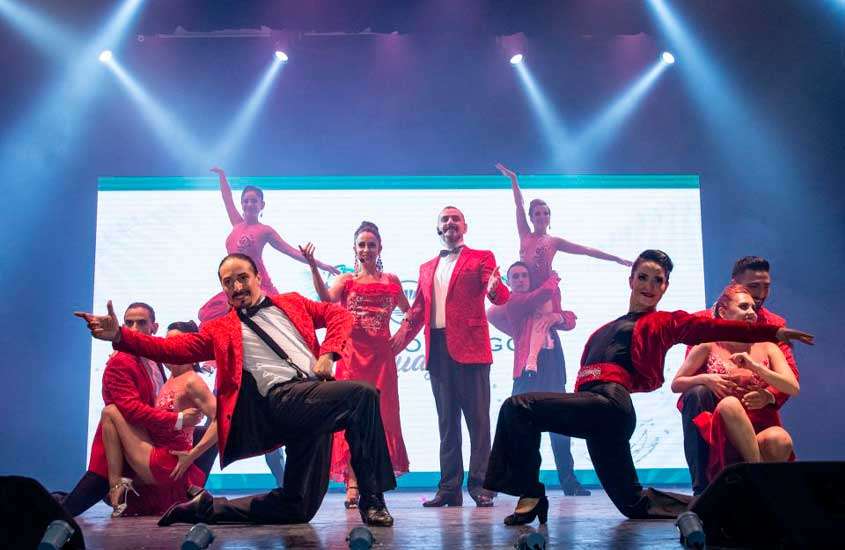 Dançarinos com roupas vermelhas durante uma apresentação de tango, iluminada por luzes brancas
