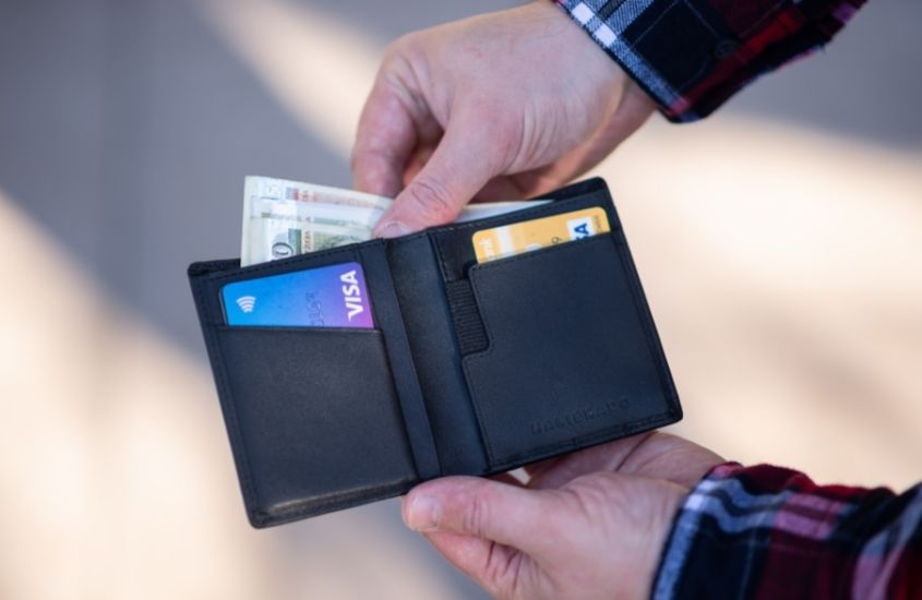 pessoa tira notas de dinheiro dentro de carteira prata onde há cartões de crédito