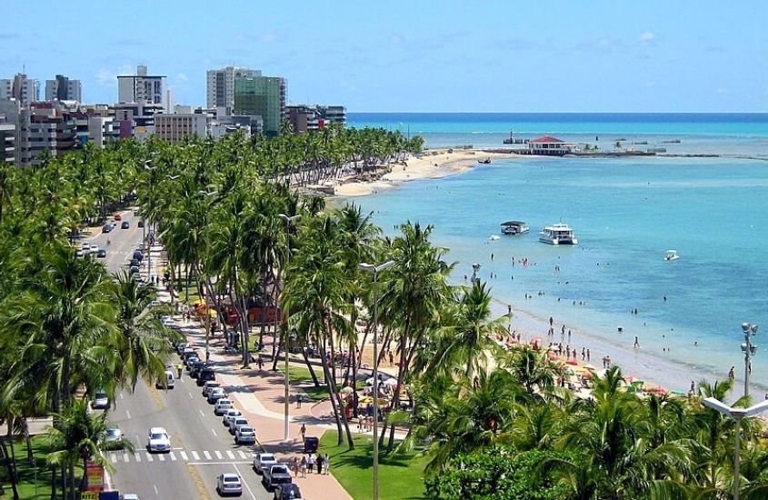 vista aérea de praia cercada de coqueiros, durante dia ensolarado em Maceió um dos melhores lugares para viajar em família no brasil