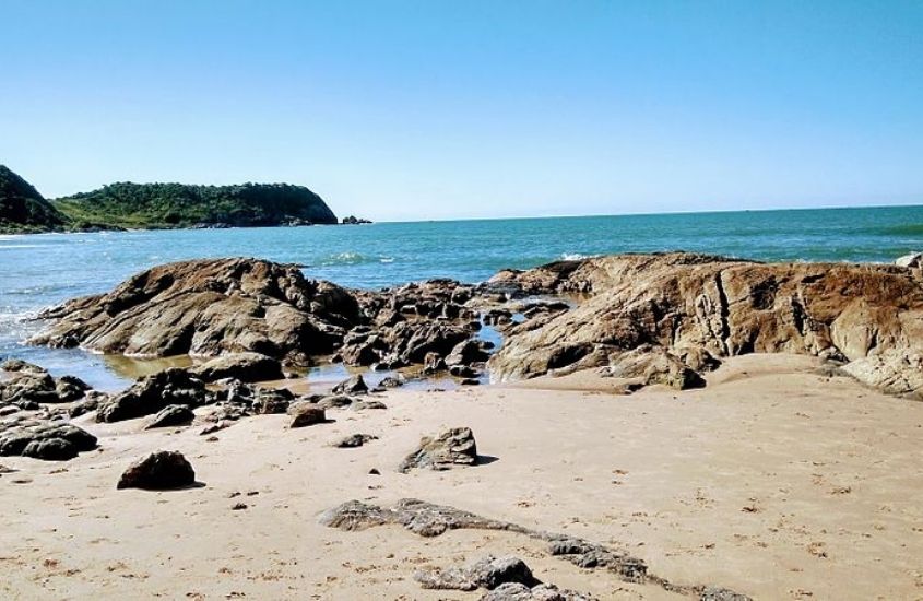 areia, pedras e mar, durante dia ensolarado em Praia em Penha SC, um dos melhores destinos para viagem em família no brasil
