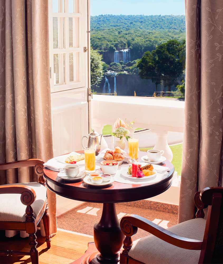 Mesa posta de café da manhã com cadeiras e janela grande do lado com paisagem das cataratas