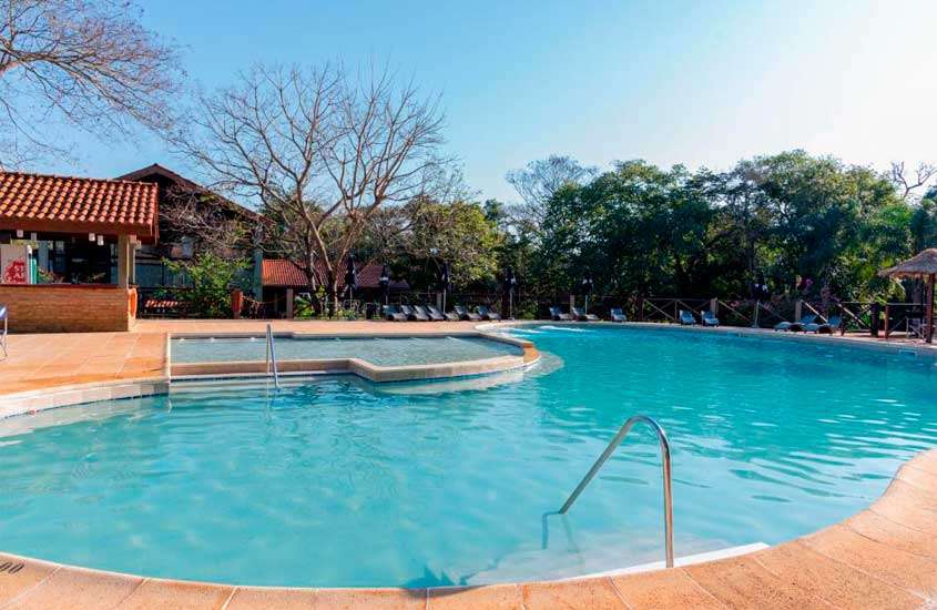 Em um dia de sol, área de lazer de um dos hotéis perto das cataratas de foz do iguaçu com piscinas, espreguiçadeiras, guarda-sóis e árvores ao redor