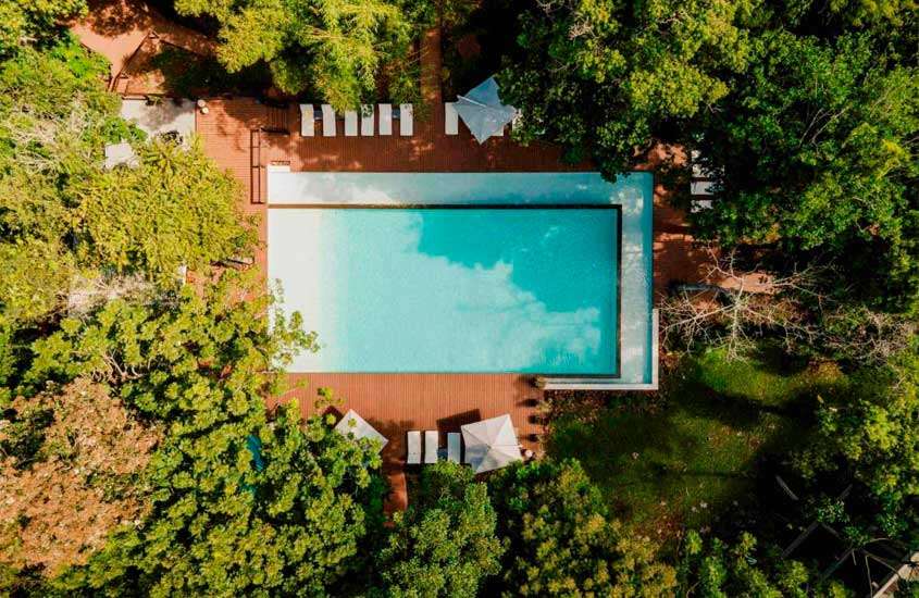Vista aérea de hotel com piscina, espreguiçadeiras, guarda-sóis e árvores ao redor