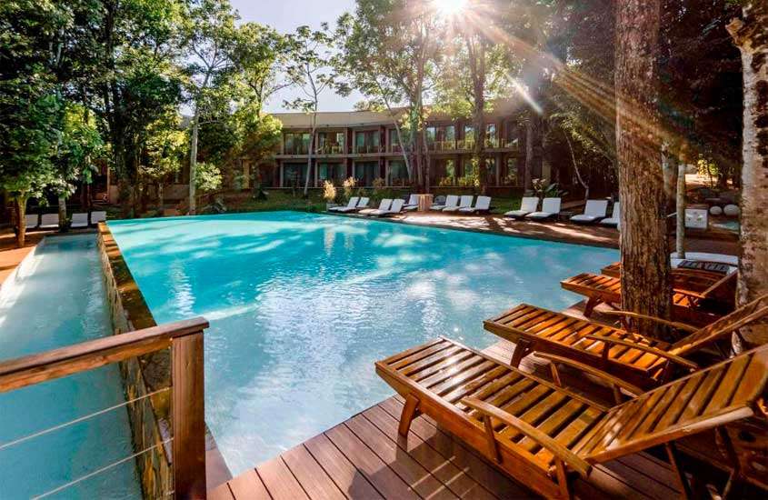Em um dia de sol, área de lazer de um dos hotéis perto das cataratas de foz do iguaçu com espreguiçadeiras e deck de madeira,piscinas, parte gramada e árvores ao redor