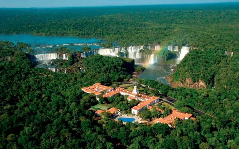 Em um dia de sol, vista aérea de hotel em foz do iguaçu perto das cataratas com cataratas atras e árvores ao redor