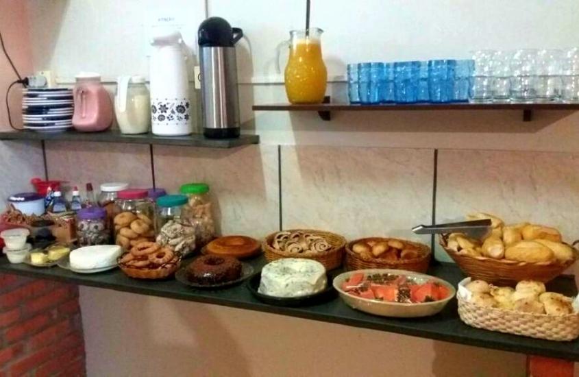 bolos, sucos, biscoitos e frutas em mesa de café da manhã de pousada aconchego do céu