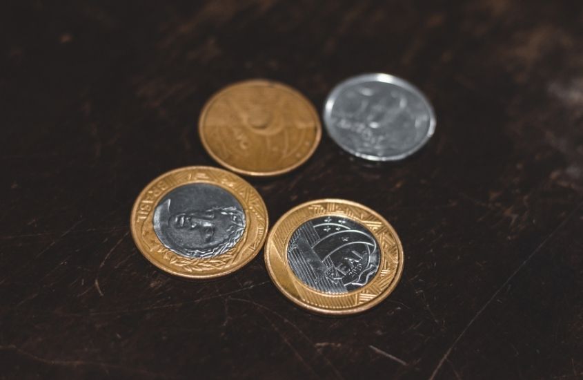moedas de 1 real, 50 centavos e 25 centavos, em cima de mesa preta