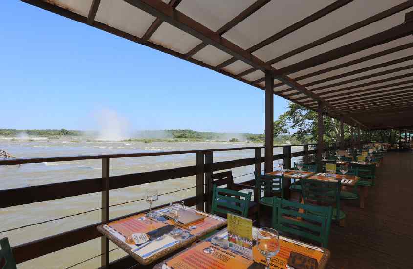 Em um dia de sol, área de alimentação de um restaurante onde comer em Foz do Iguaçu, com mesa posta e paisagem das cataratas