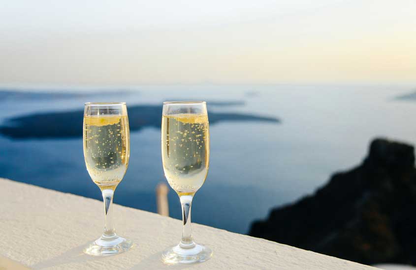 Em um final de tarde, taças de espumante com paisagem de Santorini na frente